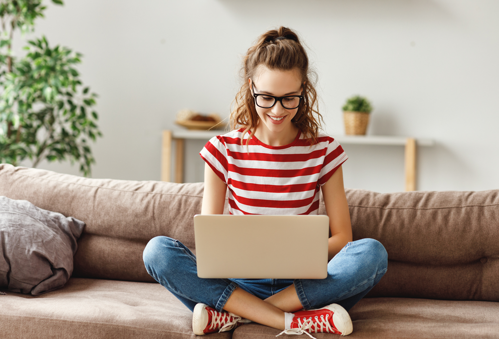 Mädchens sitzt auf der Couch und schaut auf den Laptop